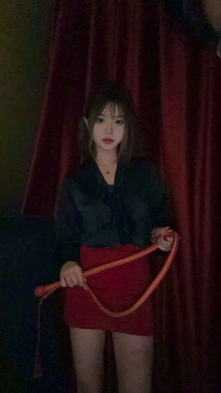 穿着红色裙子和黑色衬衫的女人,握着一根红色的鞭子。