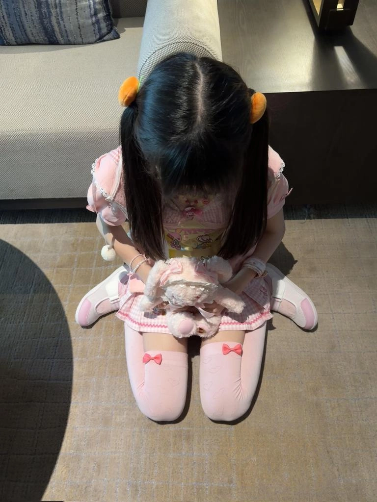穿着粉红色的裙子和白色袜子的女孩坐在椅子上。