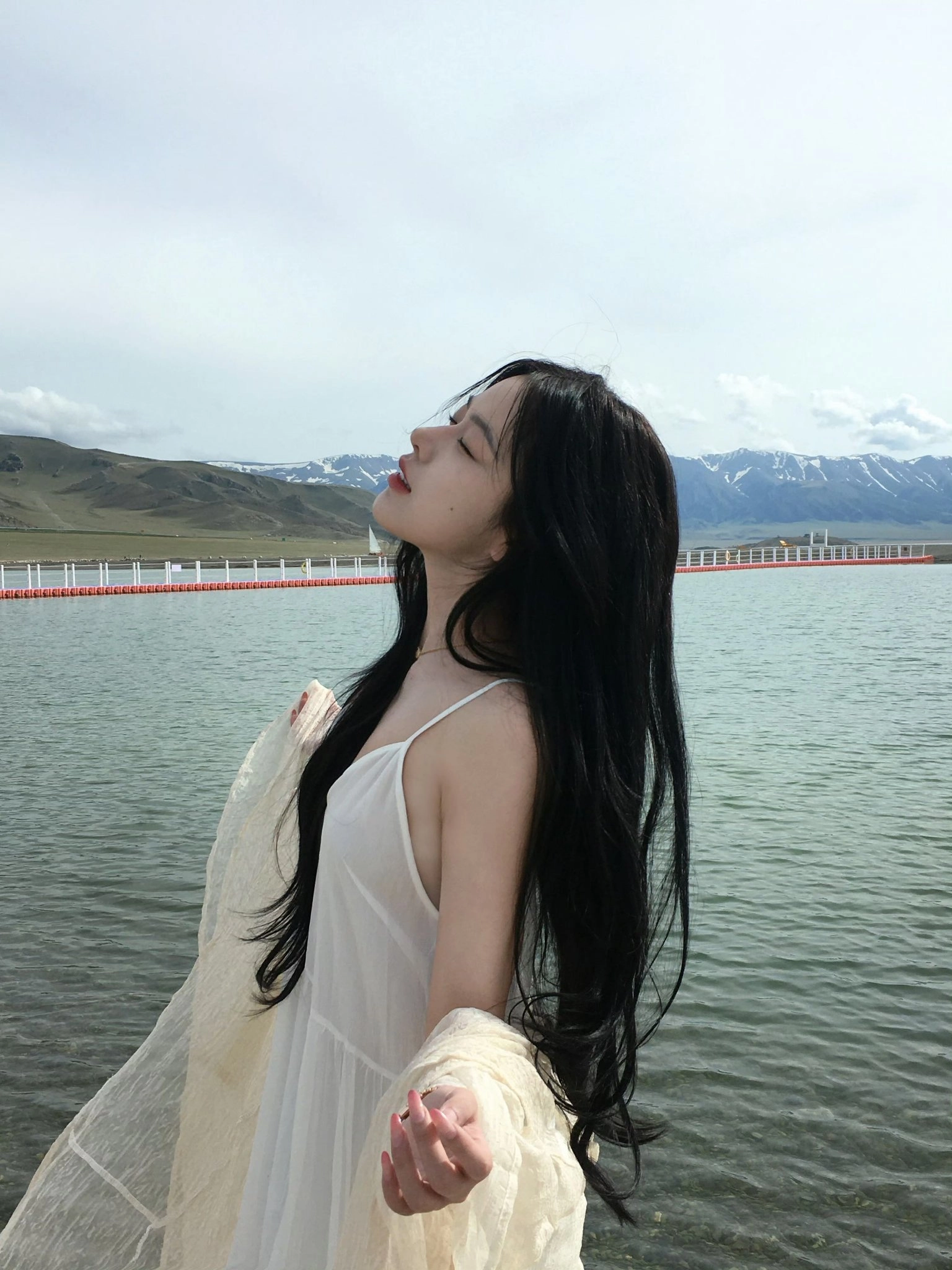 长黑头发的女人站在一个水体旁边。