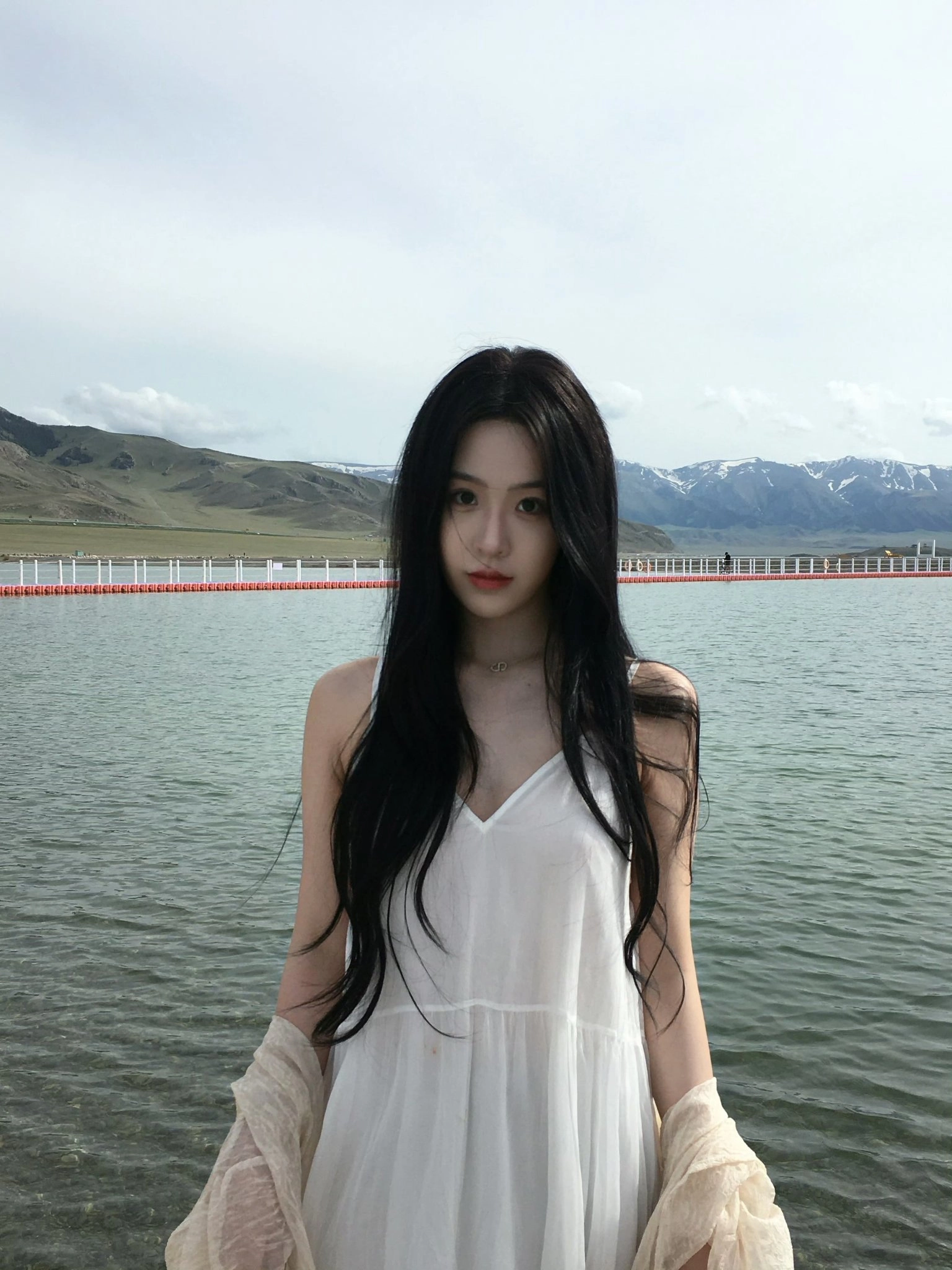 长黑头发的女人站在一个水体旁边。