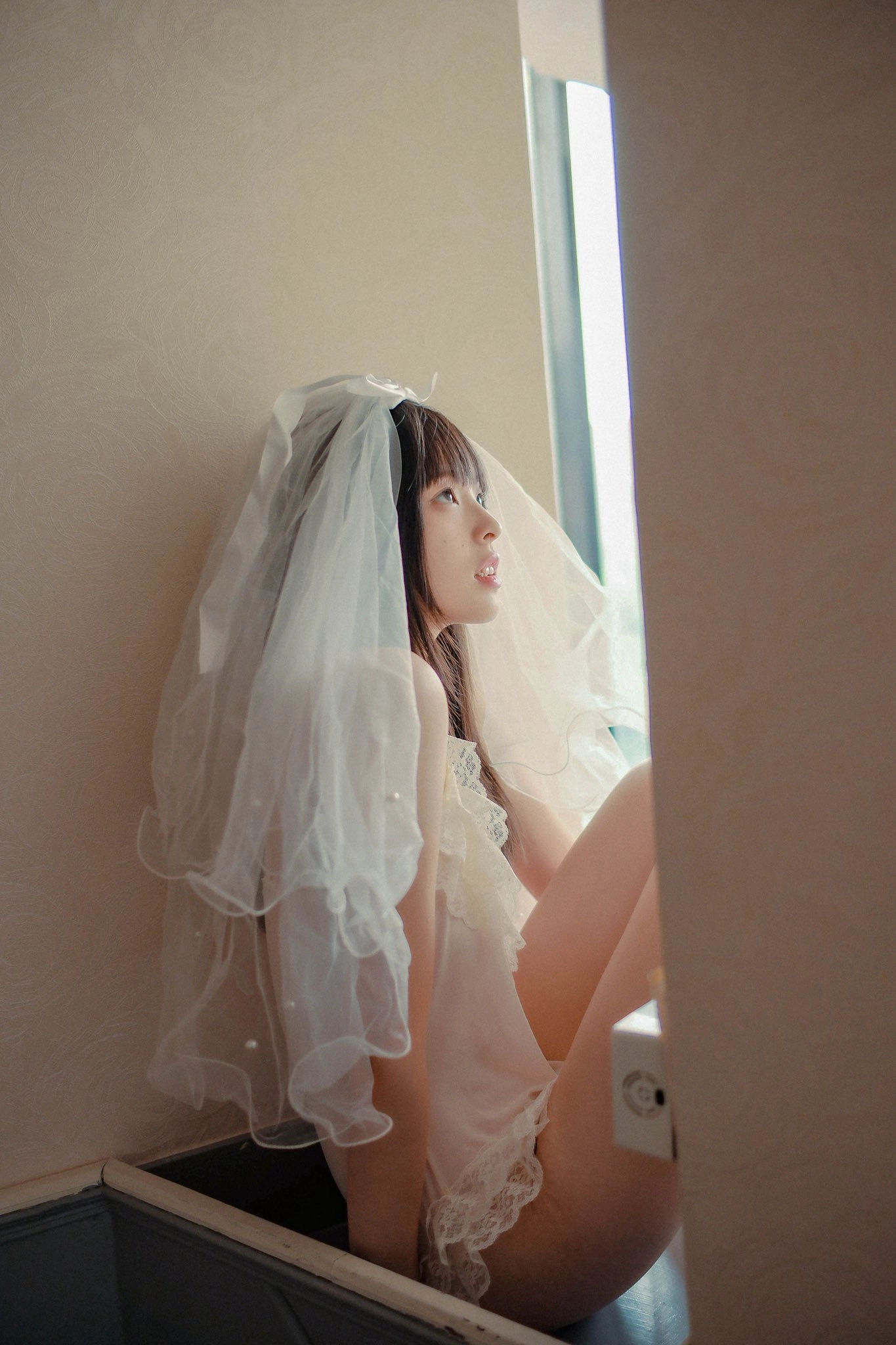 一位穿着白色裙子和面纱的女人,望着窗户。