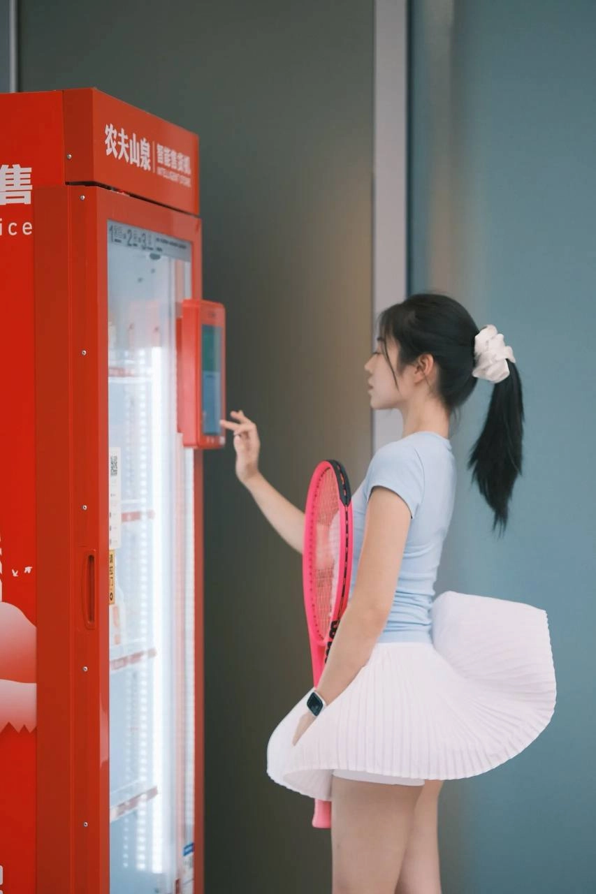 一位穿着白色衣服的女人站在一台售货机前。
