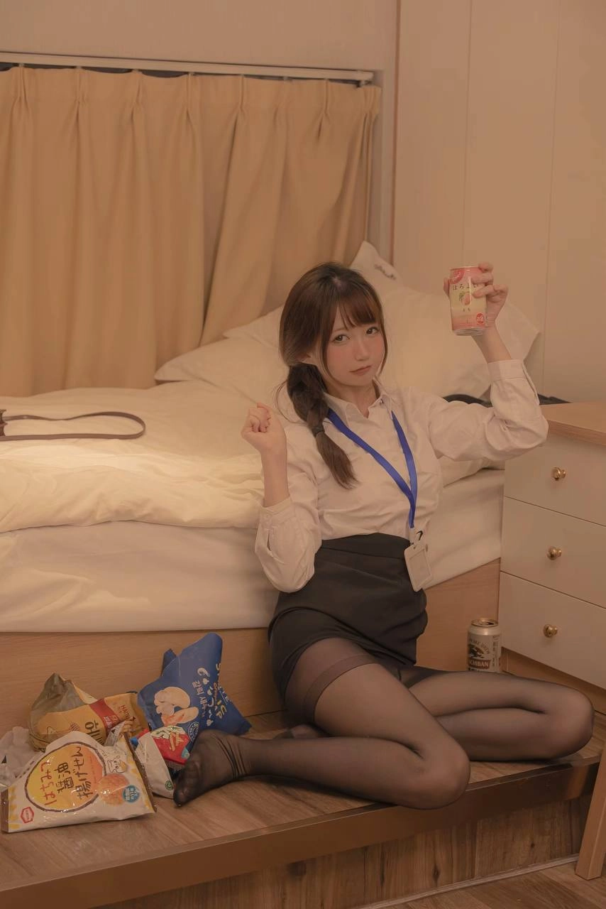 一位穿着白色衬衫和黑色裙子的女人坐在床上,拿着一罐苏打水。
